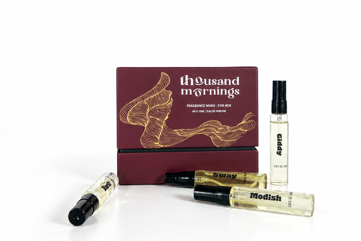 A fragrance gift set from Thousand Mornings, featuring a dark burgundy box with gold line art and text, alongside three clear glass spray bottles with black caps on a white background.