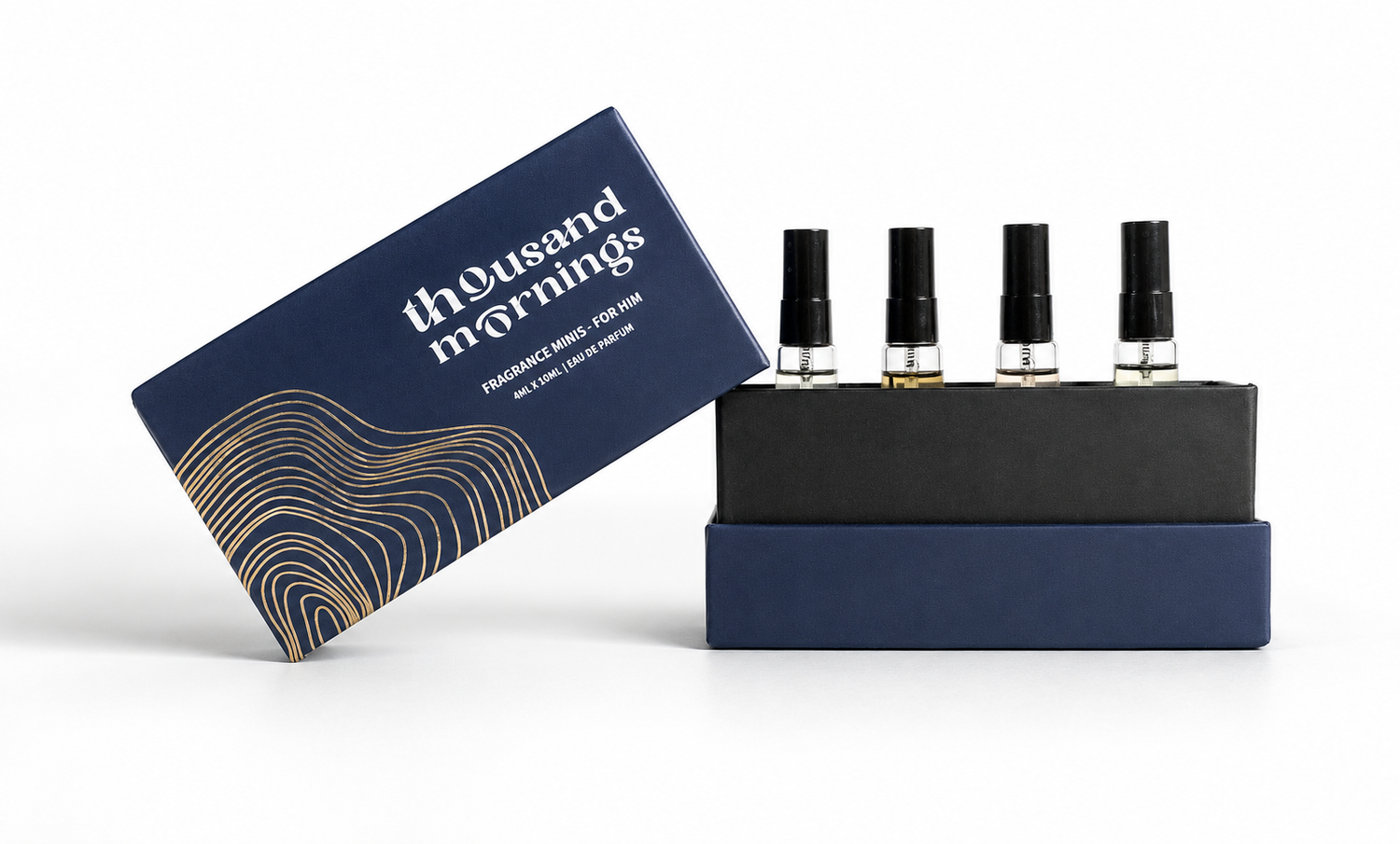 A boxed fragrance set on a clean white background, featuring a navy blue box labeled 'thousand mornings' with gold wave lines, a black tray holding four small spray bottles, and the matching navy outer box leaning beside the tray.