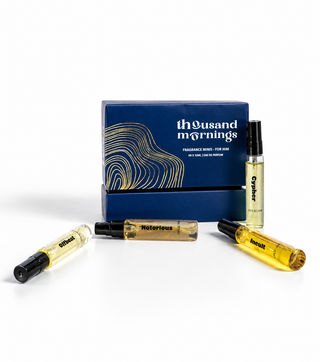 A fragrance gift set from Thousand Mornings, featuring a blue box with gold wave patterns and three clear glass spray vials containing amber-colored liquid, displayed on a clean white background.